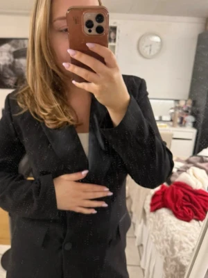 Svart kavajklänning med knappar - Säljer en svart kavajklänning med dubbelknäppning och klassisk krage. Klänningen har lång ärm och är kort i modellen, perfekt för dig som gillar en stilren och trendig look.