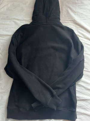 Snygg och basic Svart hoodie från Hugo boss - Säljer en svart hoodie från HUGO med gul texttryck på bröstet. Hoodien har klassisk huva med dragsko, magficka och ribbade muddar vid ärmar och nederkant. Tillverkad i mjukt sweatshirtmaterial som är skönt att bära.