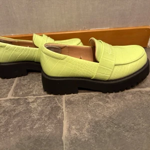 Chunky limegröna loafers - Säljer ett par chunky loafers i limegrönt med croco-mönstrad yta och kraftig svart sula. Skorna har en klassisk pennyloafers-design och är tillverkade i konstläder. 