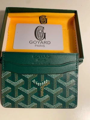 Grön korthållare från G4yard - Snygg grön korthållare från G4yard med det klassiska mönstret i vitt och gult. Tillverkad i exklusivt läder och canvas, har flera fack för kort och är perfekt för dig som vill ha något både stilrent och lyxigt. Levereras i originalask med tygpåse.