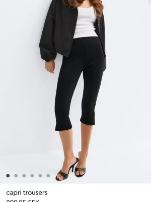 Svarta capri leggings - Stilrena svarta capri leggings med croppad längd som slutar mitt på vaden. De har en tight passform och är tillverkade i ett stretchigt material som ger en bekväm känsla. Perfekta att matcha med både sneakers och klackar för en trendig look.