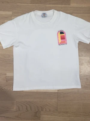 Vit Casa Blanca t-shirt med tryck - Vit t-shirt från Casa Blanca med färgglatt grafiskt tryck på bröstet och ryggen. Trycket har inslag av rosa, gul, röd och svart i ett fönsterliknande motiv. Klassisk passform och rund halsringning. Perfekt för en trendig och avslappnad stil.