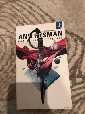 Porto Francos väktare av Ann Rosman - En spännande pocketbok av Ann Rosman, 'Porto Francos väktare', med omslag i vitt och illustration av ett svärd, tyg och havsmotiv. Boken är utgiven av Månpocket och tillhör genren spänning. Perfekt för dig som gillar deckare och historiska mysterier.