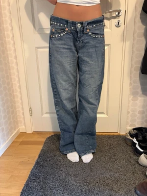 BDG (Kayla) Urban Outfitters Blå jeans med nitar och raka ben - Snygga blå jeans med raka ben och coola silverfärgade nitar längs fickor och linning. Låg midja. Storlek w 26 L32. Innerbenslängd 78cm och de är i fint skick, inte slitna nertill.
