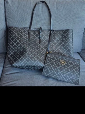 Shoppingväska By Malene Birger mönstrad - Snygg shoppingväska från By Malene Birger i svart och grått med klassiskt grafiskt mönster. Väskan har två långa handtag och kommer med en matchande clutch med dragkedja och gulddetalj. Tillverkad i tåligt konstmaterial, perfekt för dig som vill ha plats med allt.