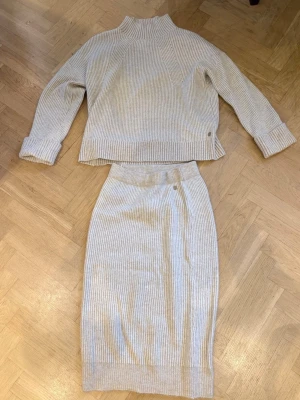 Beige ribbat stickat set - Pernilla Wahlgren - Säljer ett ribbat set i beige stickat material. Setet består av en långärmad tröja i storlek L  och en matchande kjol med resår i midjan i storlek S. (Skulle säga att det passar allt ifrån en i storlek S till L beroende på hur man vill att kläderna ska sitta). Båda delar kommer från Pernilla Wahlgrens kollektion och klädmärke🤍