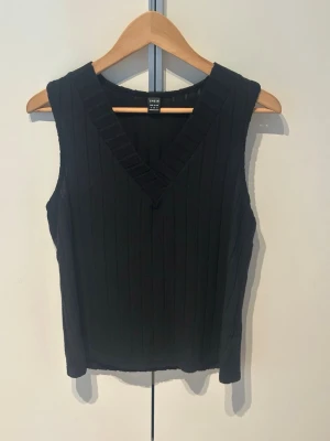 Svart ribbad linnetopp  - Svart ärmlös linnetopp med ribbad struktur och v-ringad hals. Toppen har en clean och stilren look som passar perfekt till jeans eller kjol. 