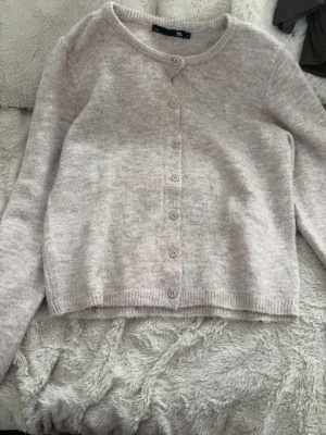 Ljusbeige stickad kofta - Mysig ljusbeige stickad kofta med rund halsringning och knappar framtill. Koftan har långa ärmar och ribbade muddar vid ärmslut och nederkant. Perfekt att slänga över en t-shirt eller linne för en skön look!💕