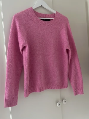 Rosa stickad tröja med rund hals - Mysig rosa stickad tröja med rund halsringning och långa ärmar. Tröjan har ribbade muddar vid ärmslut och nederkant, vilket ger en snygg och avslappnad look. Perfekt för dig som gillar färg och vill ha något bekvämt till vardagen.