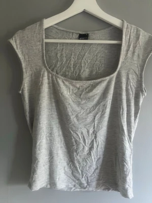 Gina tricot grå tröja  - En enkel och stilren ljusgrå linnetopp med bred urringning och ärmlös design. Tillverkad i mjuk bomull som känns skön mot huden. Perfekt att matcha med jeans eller kjol för en avslappnad look.
