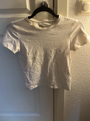 Vit kortärmad t-shirt FSBN Sister - En basic vit t-shirt från FSBN Sister i storlek XS. T-shirten har rund halsringning och korta ärmar. Tillverkad i mjuk bomull som känns skön mot huden. Perfekt att matcha med jeans eller kjol för en enkel och clean look.