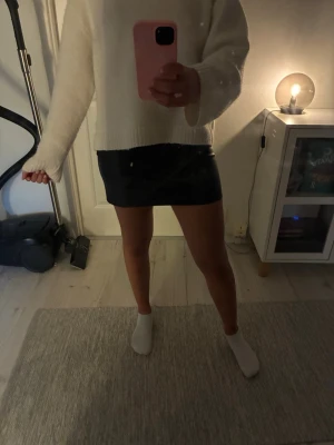 Svart minikjol i fuskskinn Kappahl - Säljer en svart minikjol i fuskskinn från Kappahl. Kjolen har en tight passform och slät yta som ger en cool och trendig look. Perfekt att styla med en stickad tröja eller crop top. Enkel dragkedja i sidan för smidig påklädning.