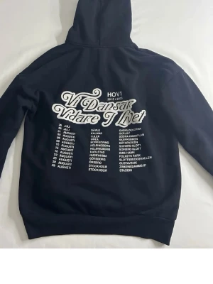 Svart Hov1 hoodie med tryck - Svart hoodie med stor vit text på ryggen 'Vi Dansar Vidare I Livet' och turnédatum. . Klassisk huva och magficka. Perfekt för dig som gillar Hov1 och vill ha en stilren och bekväm hoodie. Endast använd två ggr!