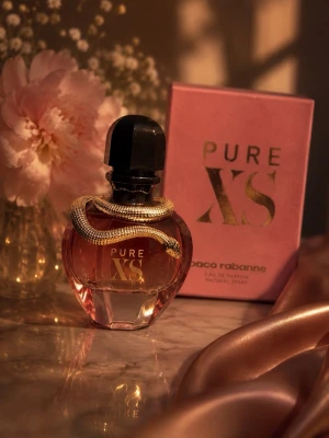 Paco Rabanne Pure XS Eau de Parfum - Lyxig parfymflaska i roséguld och svart med en dekorativ guldfärgad orm runt halsen. Flaskan har en elegant, rundad form och kommer i en rosa ask med gulddetaljer. Doften är intensiv och sensuell, perfekt för dig som vill sticka ut.
