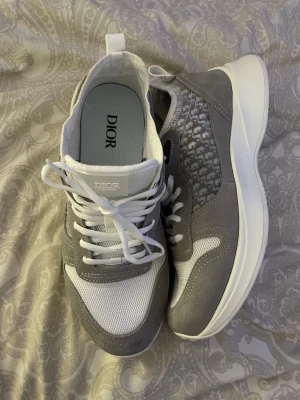 DlOE b25 - grå - strolek 45 - Snygga sneakers från DlOR i grått och vitt med ovandel i mesh och mocka. Skorna har vita snören, tjock vit sula och diskret DlOR-mönster på sidan. Perfekta för dig som vill ha en clean och exklusiv look.