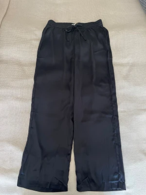 Pyjamasbyxor i satinlook - Lager 157, storlek M - nya utan prislapp - Nya utan prislapp, aldrig använda  Lager 157, Storlek M, Svarta Satin/sidenlook – mjukt, glansigt tyg (100% polyester) Resår i midjan med snörning, vida ben i avslappnad passform Längd: 107 cm fullängd Inga defekter