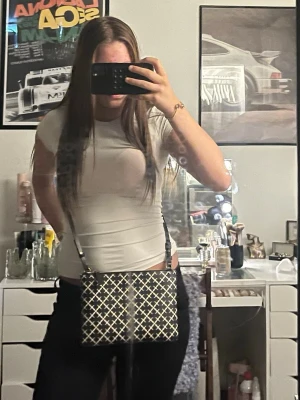 Malene Birger väska  - Snygg svart axelväska med vitt rutmönster och justerbar axelrem. Väskan har en rektangulär form och stängs upptill. Perfekt för dig som vill ha en trendig och stilren accessoar till din outfit.