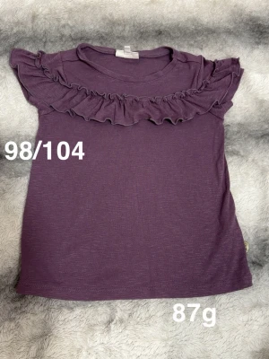 Lila topp med volangdetalj - Söt lila topp med volang längs axlar och bröst. Ärmlös modell som passar perfekt till sommaren. Mjuk och skön känsla, enkel att matcha med olika stilar.🌸Fint använt skick. Storlek 98/104