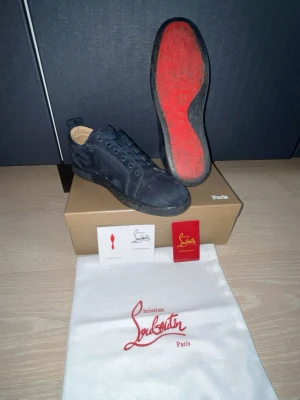 Christian Louboutin marin blåa mockaskor - Svarta sneakers i mocka från Christian Louboutin med den ikoniska röda sulan. Lågt skaft, svarta skosnören och diskret logga på sidan. Skorna levereras med originalkartong, dustbag och certifikat. Lyxig och stilren design för dig som gillar detaljer.