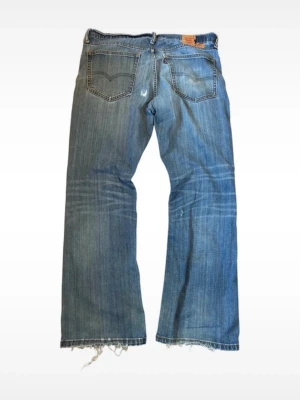 Levi's blå vintage bootcut jeans - Ett par klassiska blå bootcut jeans från Levi's med slitna detaljer och fransade benslut. Jeansen har fem fickor, synliga sömmar och en avslappnad passform. Midja 45cm