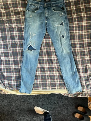 Ljusblå slitna jeans från H&M - Säljer ett par ljusblå jeans från replay med skinny fit och flera slitningar och hål på benen för en trendig, avslappnad look. Klassisk femficksmodell och dragkedja gylf. Perfekta för dig! PRIS KAN DISKUTERAS!!!