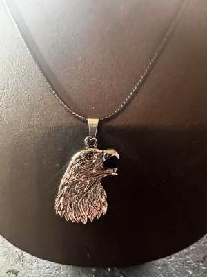 Halsband i rem - Snyggt halsband med ett detaljerat örnhuvud som hänge i silverfärgad metall. Remen är tunn och diskret vilket gör att hänget verkligen står ut. Perfekt accessoar för dig som gillar djurmotiv och vill sticka ut.