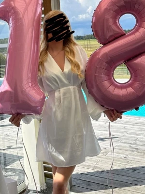 Vit omlottklänning med v-ringning - Snygg vit omlottklänning med v-ringning och långa ärmar. Klänningen har en kort längd och markerad midja, vilket ger en feminin siluett. Perfekt för sommarens tillfällen och enkel att styla med accessoarer.