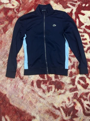 Marinblå zip-hoodie från Lacoste - Snygg marinblå zip-hoodie från Lacoste köpt på en Lacoste butik i Italien så hundra procent äkta har inget kvitto på den för fick den av min mamma i present men bara att höra av sig om funderingar.