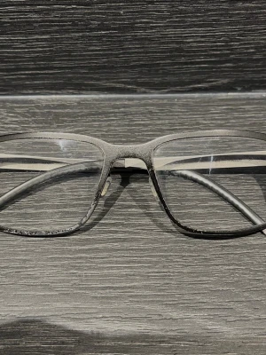 Ørgreen glasögon i titan - Kvalitetsglasögon från Ørgreen – kända för sin lätta titankonstruktion och stilrena design! Färg: Svart/silver. Mått: 58–19–152. Glasbredd: 58 mm. Bryggbredd: 19 mm. Skalmlängd: 152 mm. Bågarna säljs i begagnat skick, där färgen på bågen på sina ställen flagnat bort (se bilder för att bedöma dess skick!) Glas med styrka sitter i idag (okänd styrka) Bågen passar utmärkt för att sätta in nya glas med din egen styrka! Kika gärna in på mina andra annonser och hör av dig vid frågor och intresse!