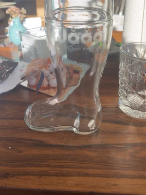 Glasstövel Jåååå by Emil Hansius - Säljer ett unikt glas format som en stövel från Jååå by Emil Hansius. Glaset är helt genomskinligt och har tryckt logga upptill. Perfekt för dig som vill sticka ut på festen eller bara ha något annorlunda i hyllan.