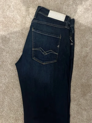 Mörkblå jeans från Replay - Snygga mörkblå jeans från Replay med klassisk femficksdesign och kontrastsömmar. Bakfickan har en unik broderad detalj och märkeslogga syns både på fickan och linningen. Perfekta för en trendig och avslappnad look.