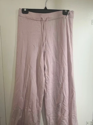 Ljusrosa mjuka loungebyxor - Superbekväma ljusrosa loungebyxor med bred resår i midjan och dragsko. Byxorna har raka, vida ben och är tillverkade i ett mjukt, stretchigt material som passar perfekt för avslappnade dagar hemma. Inga fickor eller loggor.