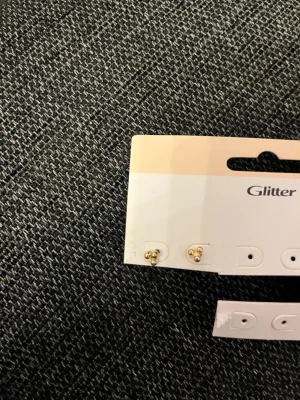 Guldiga pärlörhängen från Glitter - Säljer ett par små, guldiga örhängen från Glitter med pärldetaljer. De har en enkel och stilren design som passar perfekt till alla tillfällen. Örhängena är i metall med en glansig finish och pärlor framtill.