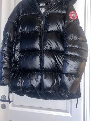 Svart dunjacka från Canada Goose - Säljer en svart, glansig dunjacka från Canada Goose med klassisk patch på ärmen. Jackan har stora, quiltade sektioner, dragkedja framtill och justerbar nederkant. Perfekt för kalla vinterdagar och riktigt varm tack vare dunfyllningen.  SKRIV TILL  Nikki77 om du är intresserad!!!