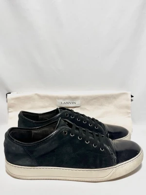 Svarta Lanvin sneakers i mocka och läder - Stilrena svarta sneakers från Lanvin med ovandel i mocka och glansig captoe! Fint skick, inga tydliga defekter. Uk 10, passar 44/45. Dustbag ingår. Kontakta mig för fler frågor och funderingar!