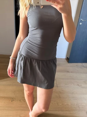 Mörkgrå ärmlös kort klänning - Snygg mörkgrå ärmlös klänning med tight passform upptill och utställd kjol. Väldigt skön att ha på sig och endast använd en gång💗