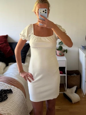 Vit kort puffärmad klänning - Superfin vit klänning med puffärmar och fyrkantig ringning. Kort modell som sitter snyggt och har en enkel, stilren design. Perfekt för dig som gillar en feminin och trendig look. Materialet känns mjukt och bekvämt mot huden.