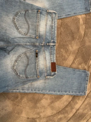 Ljusblå Lee jeans med raka ben - Säljer ett par ljusblå jeans från Lee med raka ben och klassiska femficksdetaljer. Jeansen har en snygg tvätt och Lee-logga på bakfickan. Tillverkade i bomullsdenim och stängs med dragkedja och knapp framtill.