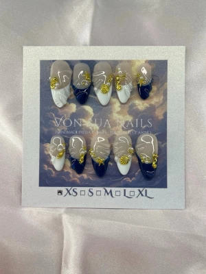 Elara (XS);Medium Almond - Snygga handgjorda press-on naglar i medium lång mandelform XS: 14 mm, 11 mm, 11,5 mm, 10 mm, 8 mm . Naglarna har en mix av marinblå och vita tippar, dekorerade med guldfärgade snäckor och pärlor samt guldpärlor. Perfekt för dig som vill ha en unik och trendig look.