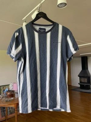 Randig t-shirt från Bondelid  M - Snygg randig t-shirt från Bondelid i blått och vitt med diskreta gröna detaljer. Klassisk rund halsringning och korta ärmar. Tillverkad i mjuk bomull som känns skön mot huden. Perfekt för en avslappnad och stilren look. Herr storlek / modell 