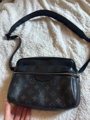 Louis Vuitton svart axelväska monogram - Snygg svart axelväska från Louis Vuitton i klassiskt monogrammönster. Väskan har justerbar axelrem, silverfärgad dragkedja och är tillverkad i tåligt läder. Perfekt för dig som vill ha en stilren och lyxig accessoar till din outfit.