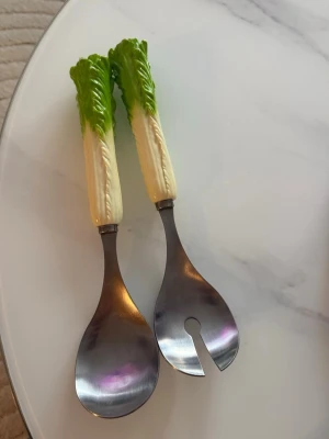 Salladsbestick med salladsbladshandtag - Unika salladsbestick i metall med handtag formade som salladsblad i grönt och vitt. Perfekta för att servera sallad på ett roligt sätt. Setet består av en salladssked och en salladsgaffel. Handtagen är detaljerade och ger ett lekfullt intryck.