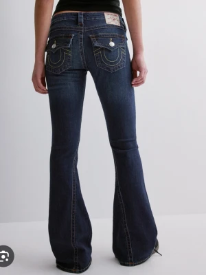 Bootcut jeans från True Religion - Mörkblå bootcut jeans från True Religion med ikoniska kontrastsömmar och snygga fickdetaljer bak. Klassisk femficksmodell med låg midja och utsvängda ben. Perfekta för en avslappnad men trendig look. Modell Joey 