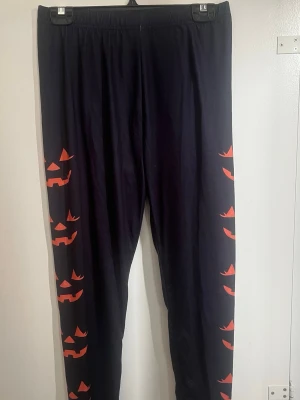 Svarta tights med pumpamönster - Coola svarta tights med orange pumpa-ansikten längs benen. Perfekta för halloween eller när du vill sticka ut lite extra. Tightsen har resår i midjan och är i stretchigt material för skön passform.