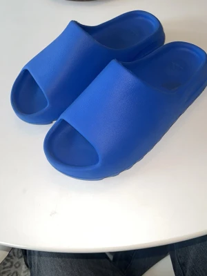 Yeezy slides blå - Säljer ett par blåa Adidas Yeezy slides tofflor i mjukt skummaterial. I jätte bra skick.