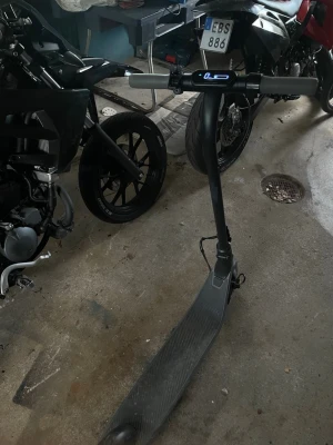 Svart elscooter med digital display - Säljer en svart elscooter med stilren design och digital display på styret som visar hastighet och batterinivå. Scootern har bred fotplatta med mönstrad yta för bättre grepp och robusta hjul. Perfekt för smidig transport i stan.