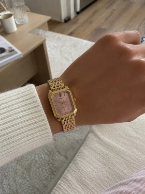 Guldig klocka med rosa urtavla - Snygg klocka med fyrkantig, rosa urtavla och guldfärgat metallarmband. Klockan har minimalistiska index och en elegant design som passar perfekt till din stil. Lätt att matcha med olika outfits och ger en lyxig känsla på handleden.