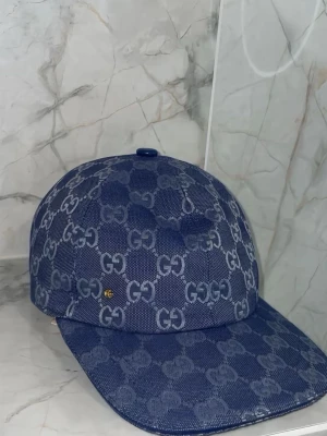 Blå keps med monogram - Säljer en blå keps med det klassiska monogrammet över hela kepsen. Kepsen har böjd skärm och är tillverkad i ett slitstarkt tygmaterial. Perfekt för dig som vill ha en stilren accessoar med lyxig känsla.