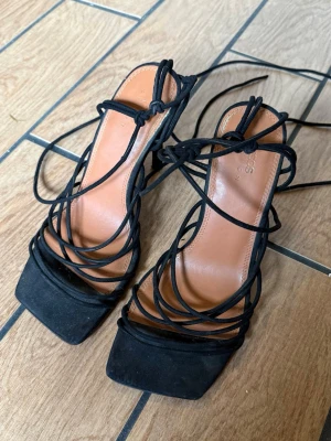 Svarta klackskor med snörning från ASOS - Trendiga svarta pumps från ASOS med höga klackar och snygga snörningsdetaljer som går att vira runt vristen och upp på benet, Skorna har fyrkantig tå, ovandel i mockaimitation och brun innersula i konstläder. Perfekt för dig som gillar att sticka ut.