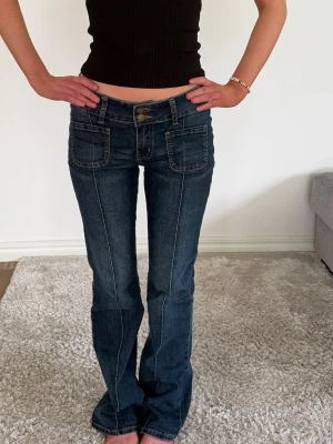 Mörkblå bootcut jeans med fickor - Snygga mörkblå bootcut jeans med stora framfickor och markerade sömmar. Jeansen har låg midja och klassiska bakfickor med lock och knapp. Perfekta för en trendig och avslappnad look.